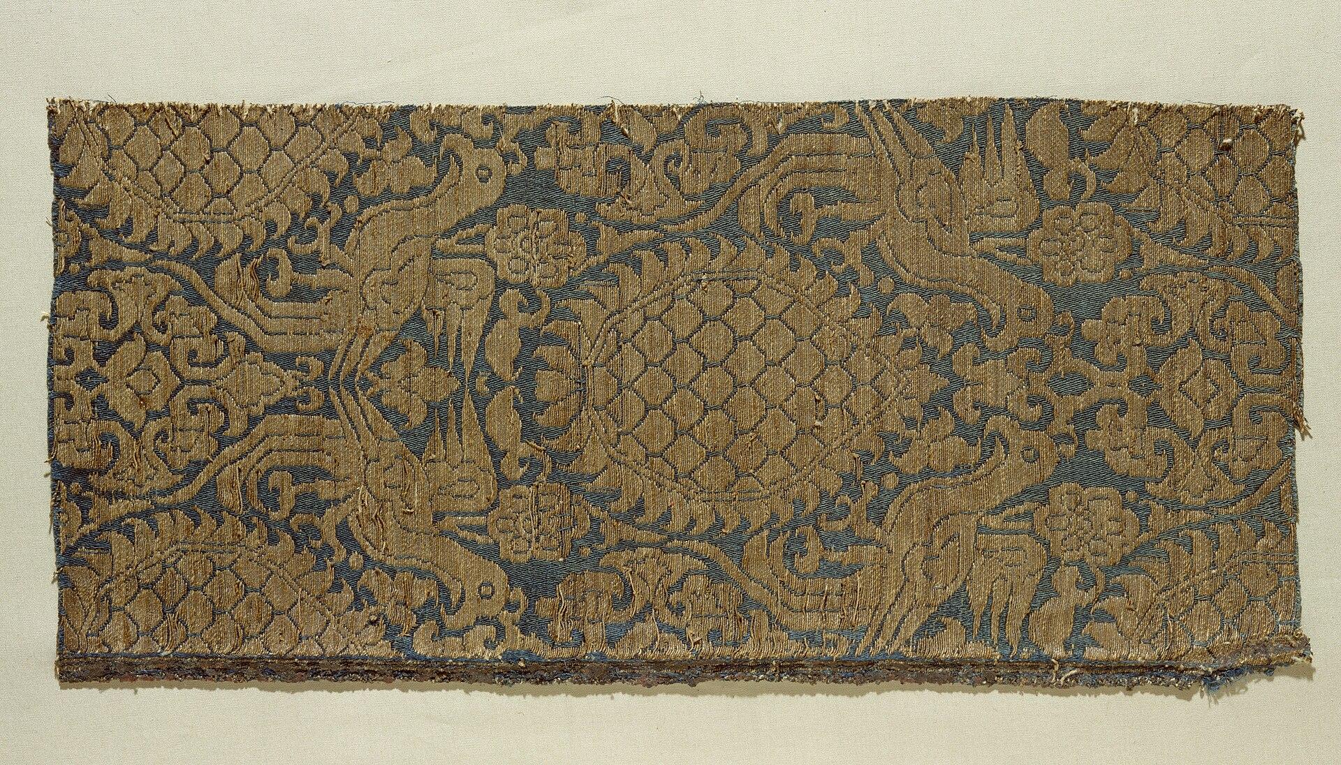 Mittelalterliches Seidenfragment mit goldfarbenem Pflanzen- und Tiermuster auf blauem Grund